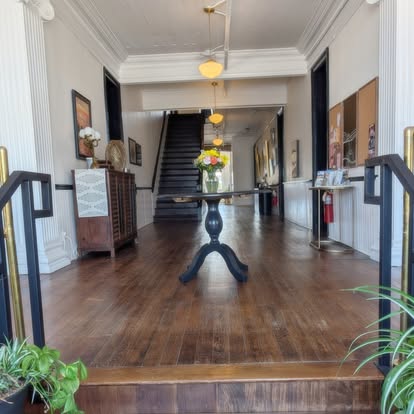 Hattie House front hall with a pedestal table of flowers and the staircase beyond