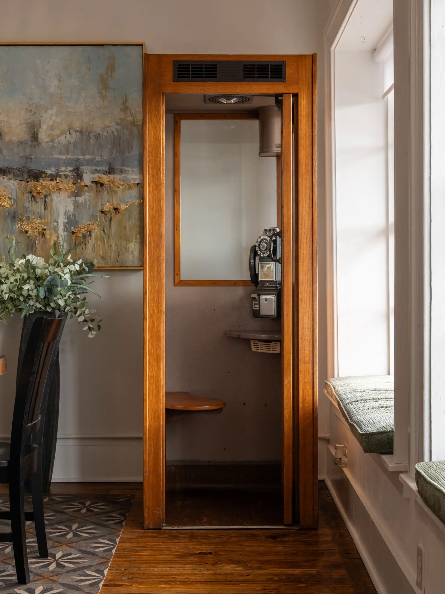 Restored wooden telephone booth beside original artwork and window seating