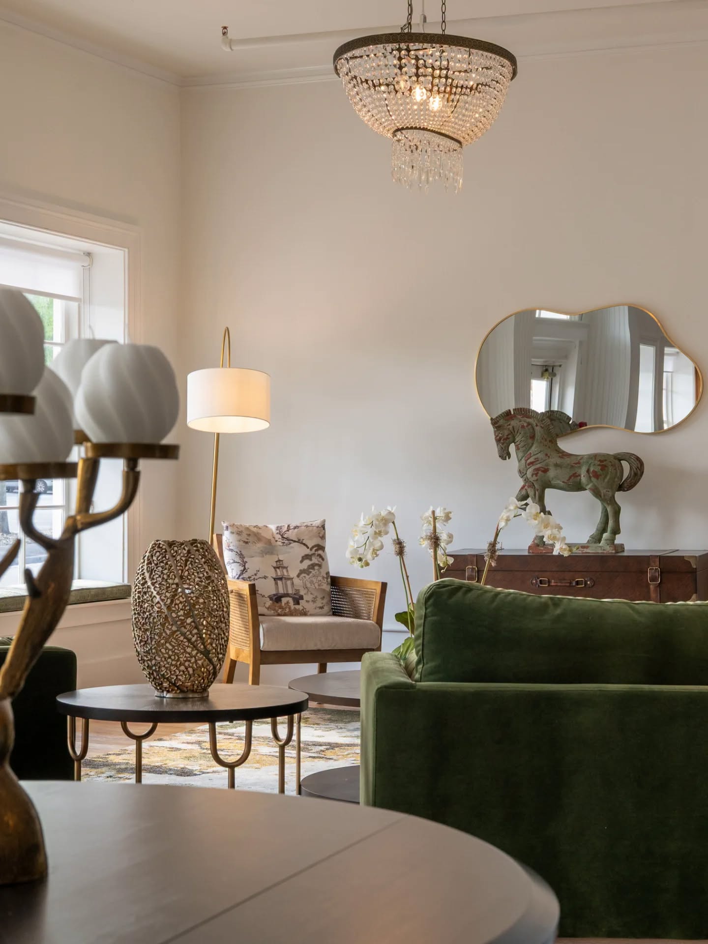 Hattie House front lounge with a moss green velvet sofa, tiered crystal chandelier, and gilded mirror