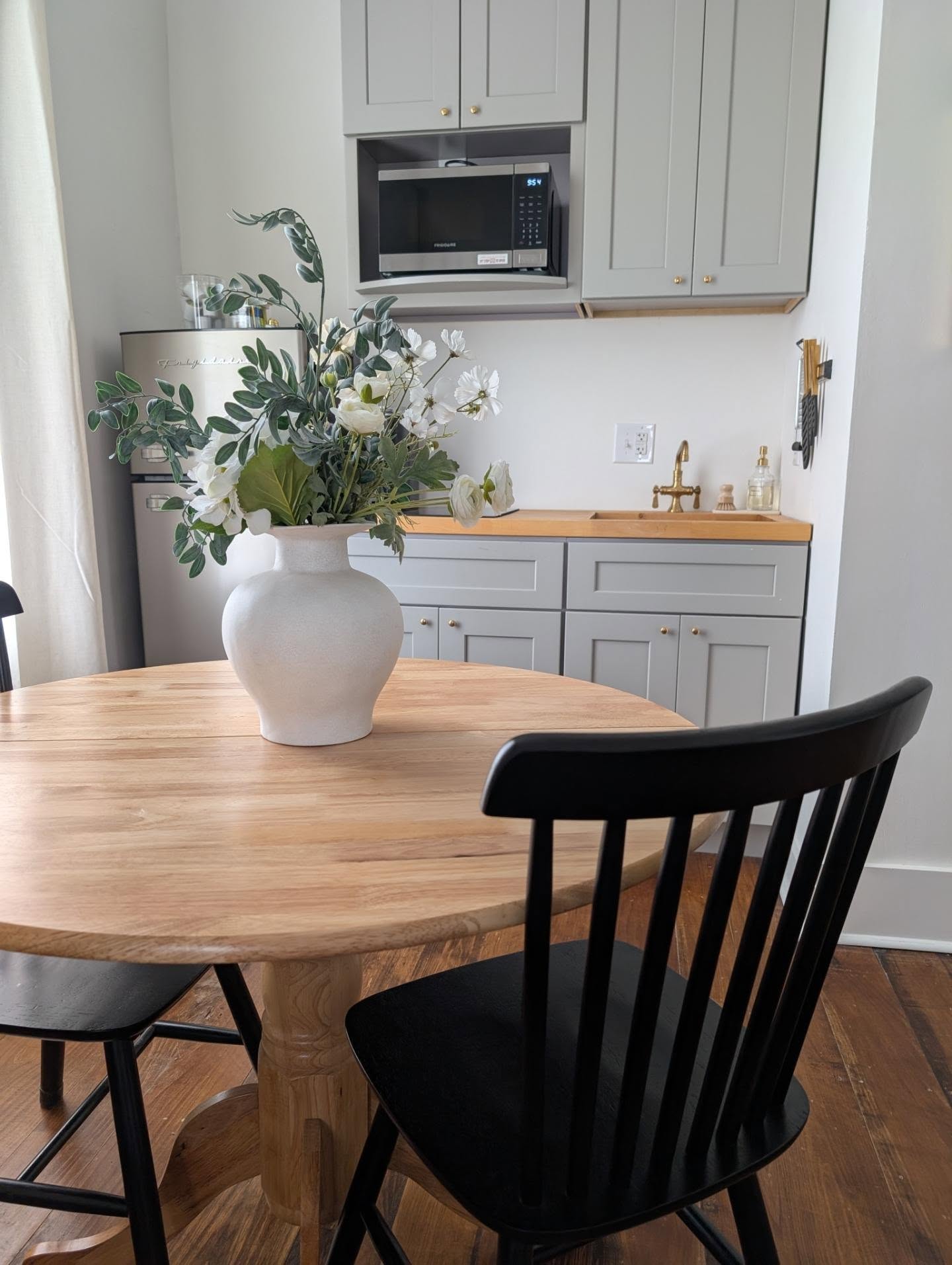 Suite kitchenette with round dining table, grey cabinetry, brass faucet, and microwave