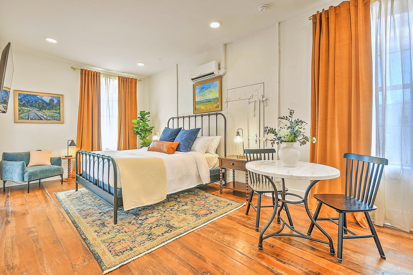 King Suite with iron bed, original wood floors, orange drapery, and sitting area