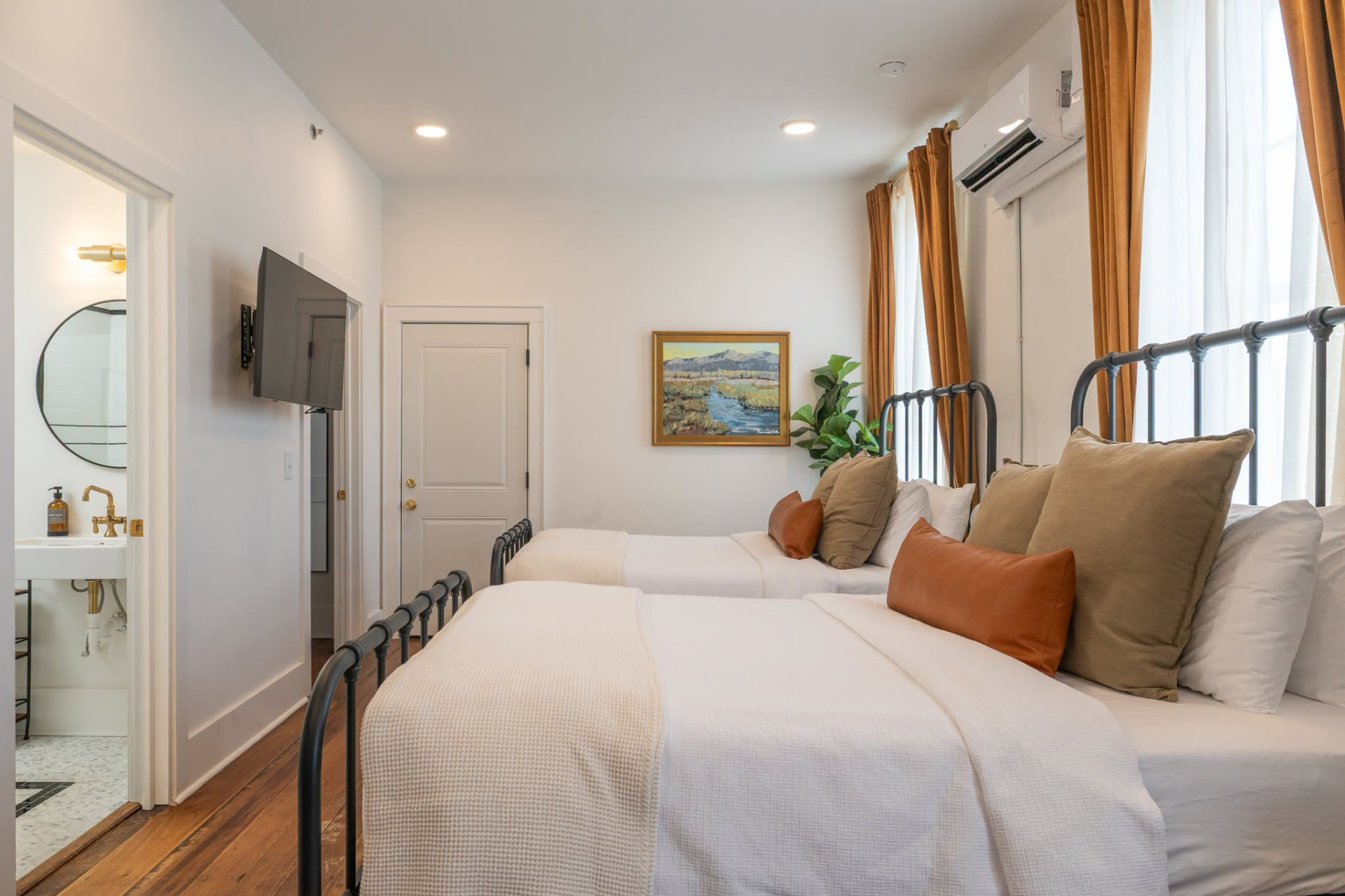 Double Queen Suite with two iron beds, tall windows, original wood floors, and private bathroom
