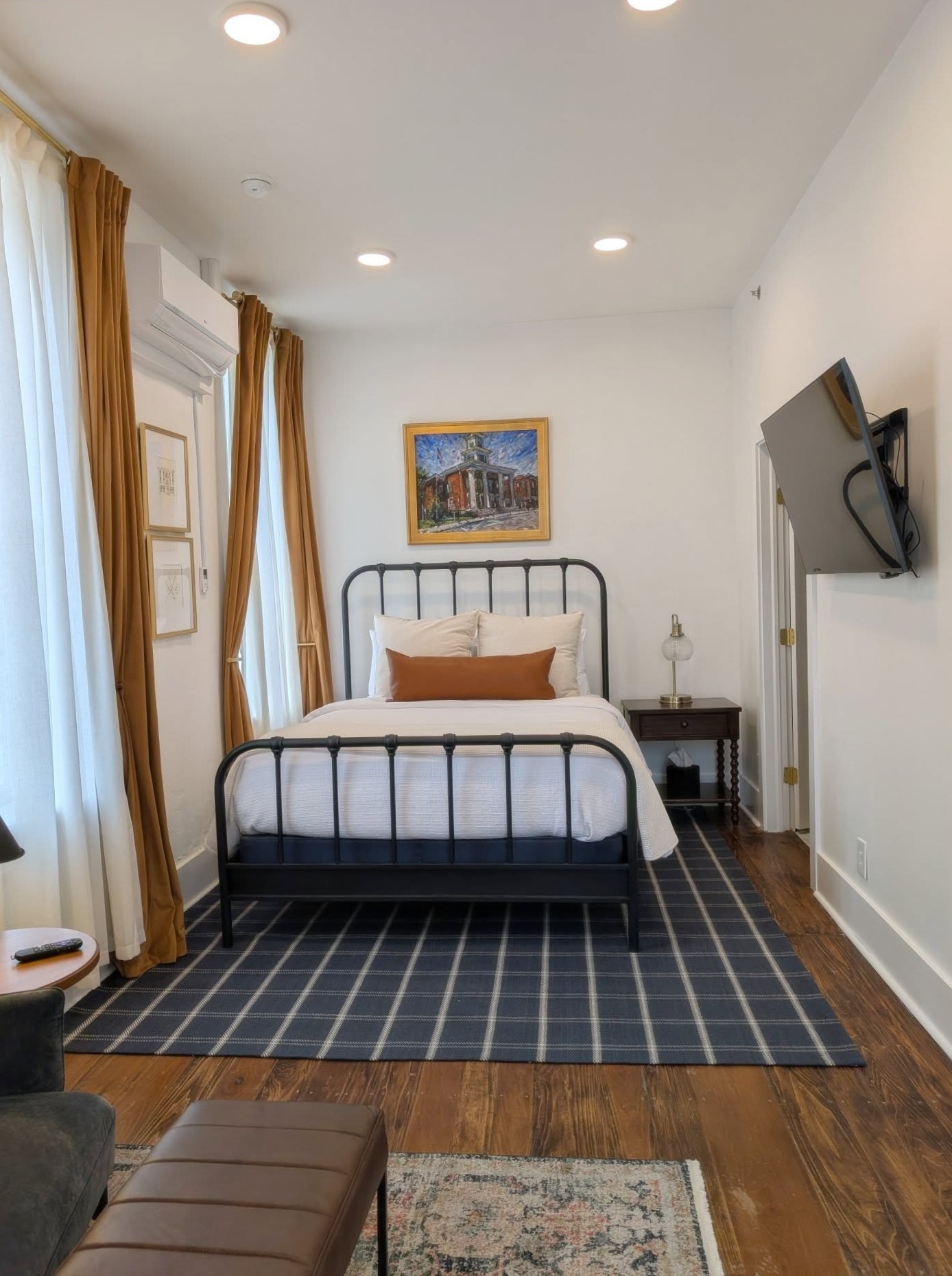 Queen Suite with a single iron bed, tall windows, original wood floors, and artwork